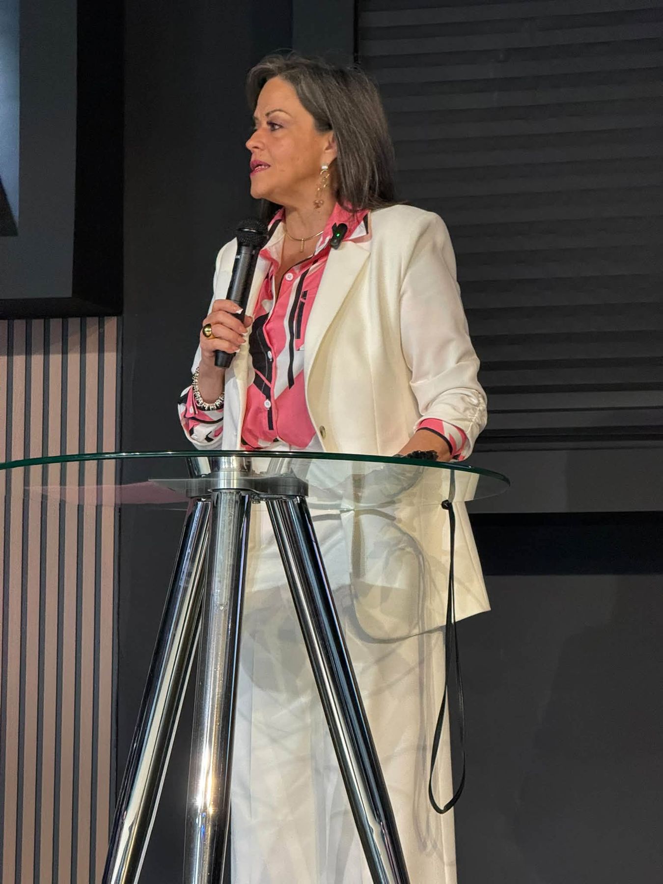 Predicadora con blazer blanco hablando desde el púlpito de cristal