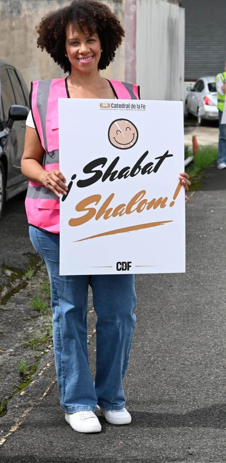 Voluntaria del equipo de bienvenida sonriendo con un letrero de Shabat Shalom